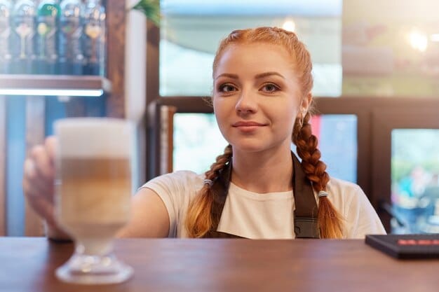 A person confidently paying for coffee at a cafe using facial recognition on their mobile phone. The barista smiles in the background, reflecting the ease and speed of the transaction.