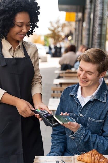 A cashier using a digital payment terminal with a customer tapping their smartphone to make a payment, illustrating a quick and seamless transaction.