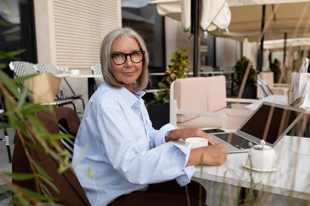 An elderly woman with glasses is at a small business counter, smiling as she uses her smartphone to make a digital payment with the help of a friendly store clerk. The store is well-lit and welcoming, with shelves filled with local products.
